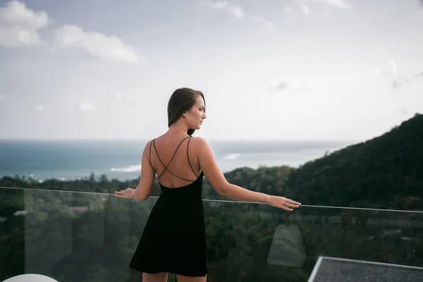 ドレスを着た美しい女の子は ワインと帽子が太陽からカバーを取ってプールのそばの豪華なヴィラで休んでいます ヤシの木と海の眺め サムイ島 — ストック写真