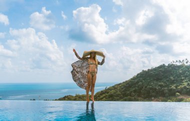 Mayo giymiş güzel bir kız, rüzgarda gelişen bir şapka ve bornoz, havuzu ve ormanın ve denizin güzel manzarası olan bir villada duruyor. Tayland, Samui