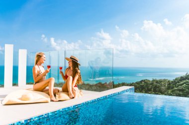 Güzel kızlar havuz kenarında şarapla eğleniyorlar ve seyahat ve hafta sonundan bahsediyorlar. 8 Mart 'ta görüşelim. Tatiller ve deniz kenarındaki bir villada havuz başında partiler. Tayland, Samui