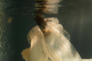 Güzel kız uzun saçlarıyla su altında yüzer. Altın gibi mavi ya da altın arkaplan. Bir peri masalı ya da büyünün atmosferi. Parlak bir bezle suyun altına dalıyorsun.