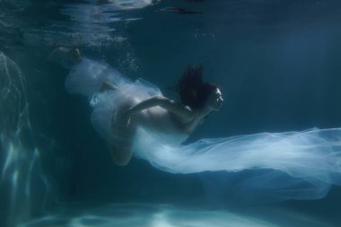 Güzel kız uzun saçlarıyla su altında yüzer. Altın gibi mavi ya da altın arkaplan. Bir peri masalı ya da büyünün atmosferi. Parlak bir bezle suyun altına dalıyorsun.