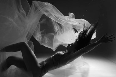 Güzel kız jimnastikçi ve sporcu kadın havuzda parlak kumaşlarla suyun altında yüzüyor.