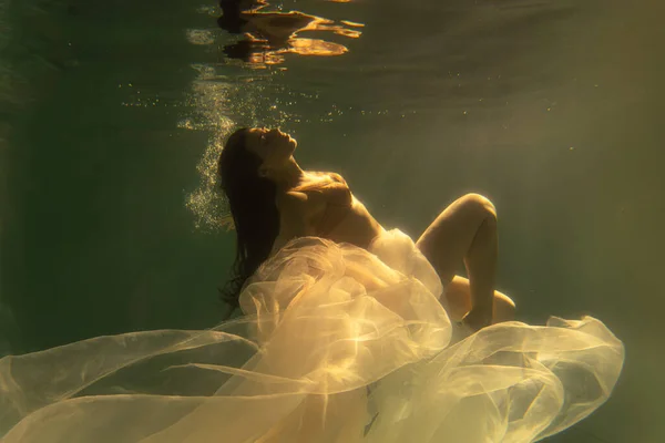 美しい少女は長い髪で水中で泳ぐ 金のような青や金の背景 おとぎ話や魔法の雰囲気 光沢のある布で水中でのダイビング — ストック写真