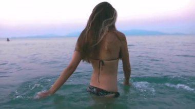 Güzel, ince ve genç bir kız turkuaz denizde yüzüyor. Uzun saç ve modelde ince bir figür. Bir kadın suya dalıyor ve su sıçrıyor. Sakinlik, mutluluk ve rahatlama kavramı..