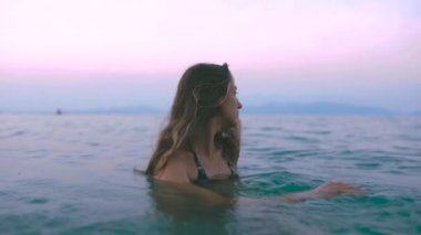 Güzel, ince ve genç bir kız turkuaz denizde yüzüyor. Uzun saç ve modelde ince bir figür. Bir kadın suya dalıyor ve su sıçrıyor. Sakinlik, mutluluk ve rahatlama kavramı..