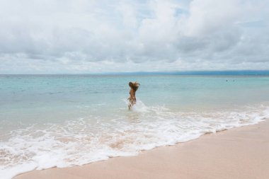 Mavi dalgalarla okyanus ve denizde poz veren mayolu güzel ve genç bir kız. Mayo mankenli ve moda pozu veren bir kadın. Bali adasında rahatla ve rahatla.