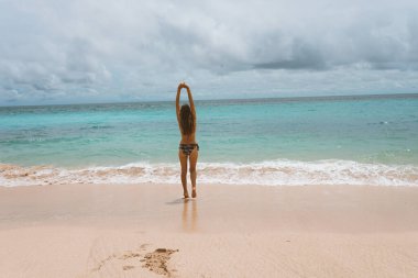 Mavi dalgalarla okyanus ve denizde poz veren mayolu güzel ve genç bir kız. Mayo mankenli ve moda pozu veren bir kadın. Bali adasında rahatla ve rahatla.
