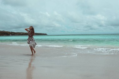 Okyanus ve denizin kıyısında mavi dalgalarla poz veren güzel ve genç bir kız. Uzun elbise mankeni ve moda pozu giymiş bir kadın. Bali adasında rahatla ve rahatla.