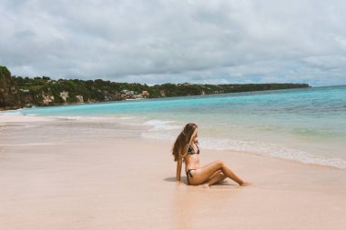 Mavi dalgalarla okyanus ve denizde poz veren mayolu güzel ve genç bir kız. Mayo mankenli ve moda pozu veren bir kadın. Bali adasında rahatla ve rahatla.