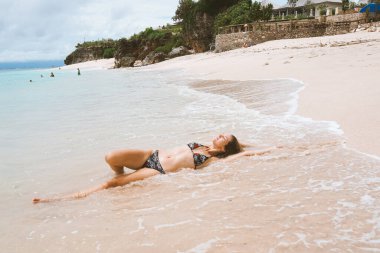 Mavi dalgalarla okyanus ve denizde poz veren mayolu güzel ve genç bir kız. Mayo mankenli ve moda pozu veren bir kadın. Bali adasında rahatla ve rahatla.