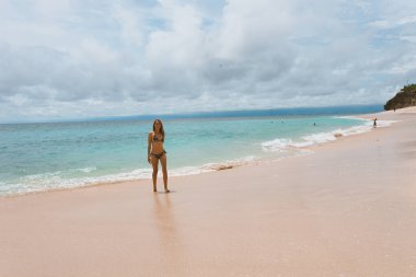 Mavi dalgalarla okyanus ve denizde poz veren mayolu güzel ve genç bir kız. Mayo mankenli ve moda pozu veren bir kadın. Bali adasında rahatla ve rahatla.