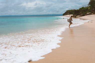 Okyanus ve denizin kıyısında mavi dalgalarla poz veren güzel ve genç bir kız. Uzun elbise mankeni ve moda pozu giymiş bir kadın. Bali adasında rahatla ve rahatla.