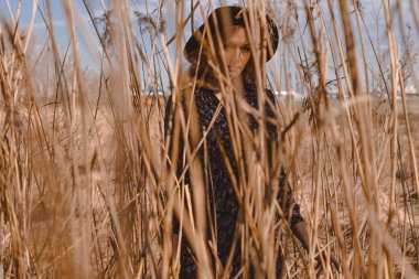 Kırsalda elbise giymiş güzel bir kız. Bir tarlanın arka planına ve buğday arasında yüksek voltajlı kablolara karşı. Mavi gökyüzü ve model