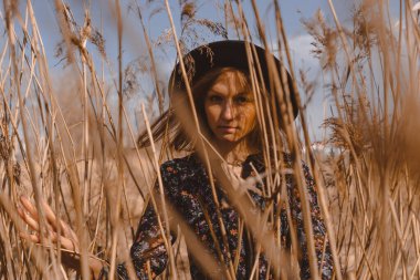 Kırsalda elbise giymiş güzel bir kız. Bir tarlanın arka planına ve buğday arasında yüksek voltajlı kablolara karşı. Mavi gökyüzü ve model