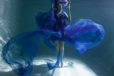 Mavi elbiseli güzel kız havuzda ya da denizde yüzüyor..