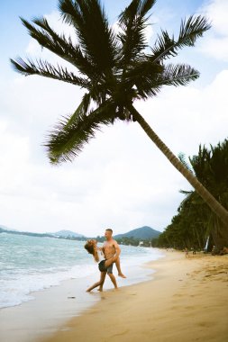 Güzel erkek ve kız koşar ve okyanusta veya denizde sahilde eğlenirler. Karı kocanın tropiklerinde balayı. Ateşli ülkelerde aşk. Kumda yuvarlan ve mutlu ve aşık ol. Aşıklar