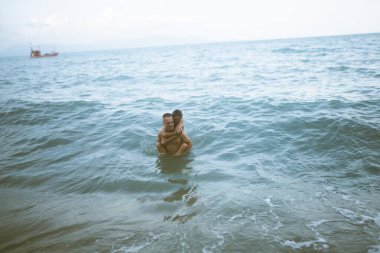 Güzel erkek ve kız koşar ve okyanusta veya denizde sahilde eğlenirler. Karı kocanın tropiklerinde balayı. Ateşli ülkelerde aşk. Kumda yuvarlan ve mutlu ve aşık ol. Aşıklar