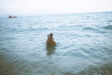 Güzel erkek ve kız koşar ve okyanusta veya denizde sahilde eğlenirler. Karı kocanın tropiklerinde balayı. Ateşli ülkelerde aşk. Kumda yuvarlan ve mutlu ve aşık ol. Aşıklar