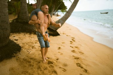 Güzel erkek ve kız koşar ve okyanusta veya denizde sahilde eğlenirler. Karı kocanın tropiklerinde balayı. Ateşli ülkelerde aşk. Kumda yuvarlan ve mutlu ve aşık ol. Aşıklar