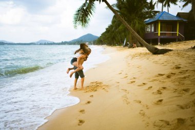Güzel erkek ve kız koşar ve okyanusta veya denizde sahilde eğlenirler. Karı kocanın tropiklerinde balayı. Ateşli ülkelerde aşk. Kumda yuvarlan ve mutlu ve aşık ol. Aşıklar