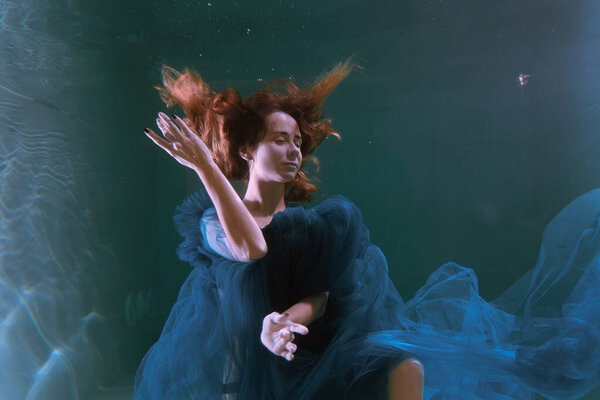 Beautiful girl in a blue dress swims underwater in the pool or in the sea.