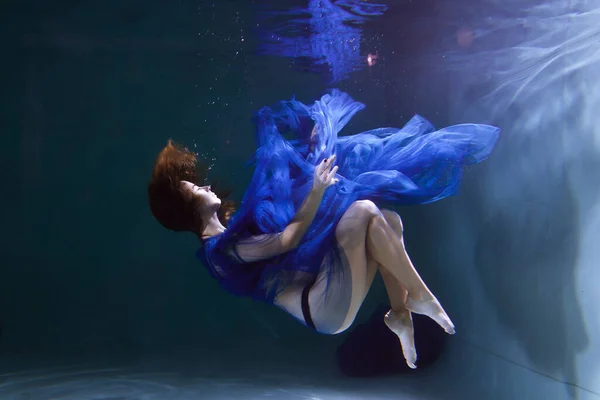 身穿蓝色衣服的漂亮姑娘在水里或海里游泳 免版税图库照片