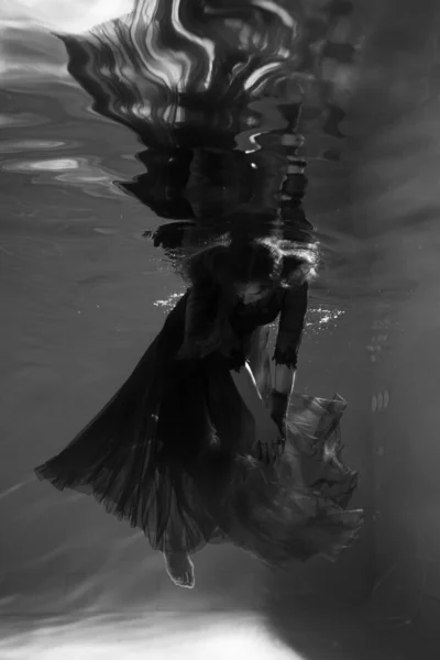 Beautiful girl underwater in a red dress swims in the pool. Tenderness and elegance. Bubbles and a lot of water