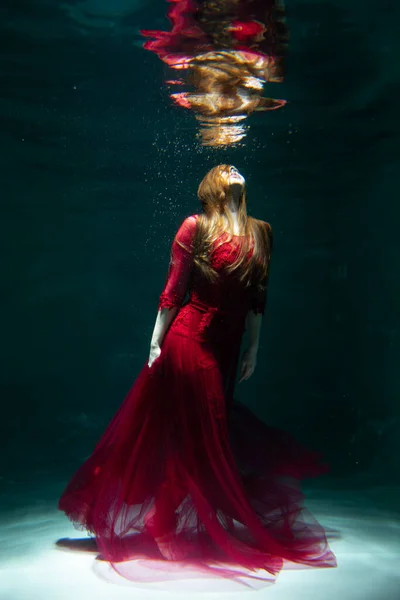 身穿红色衣服的漂亮女孩在游泳池里游泳 温柔和优雅 泡泡和大量的水 图库照片