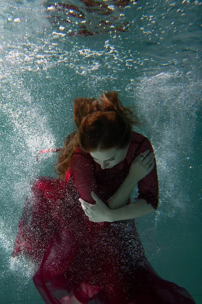 身穿红色衣服的漂亮女孩在游泳池里游泳 温柔和优雅 泡泡和大量的水 免版税图库图片