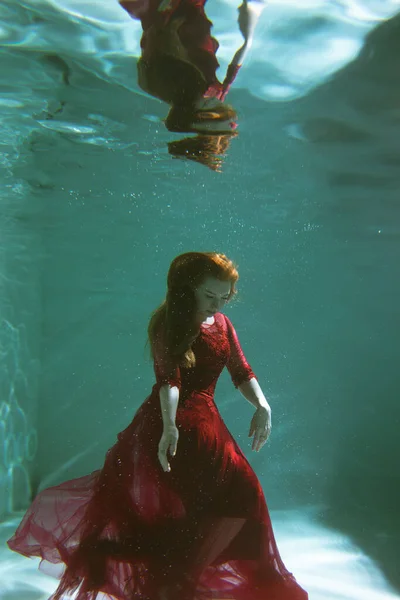身穿红色衣服的漂亮女孩在游泳池里游泳 温柔和优雅 泡泡和大量的水 图库图片