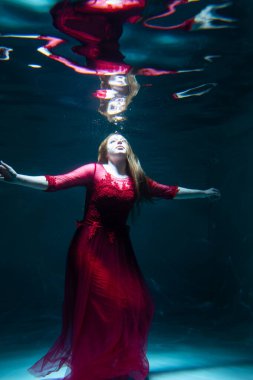 Kırmızı elbiseli güzel bir kız havuzda yüzüyor. Şefkat ve zarafet. Baloncuklar ve bolca su.