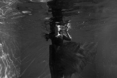 Kırmızı elbiseli güzel bir kız havuzda yüzüyor. Şefkat ve zarafet. Baloncuklar ve bolca su.