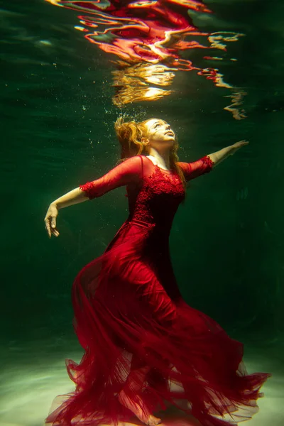 身穿红色衣服的漂亮女孩在游泳池里游泳 温柔和优雅 泡泡和大量的水 免版税图库照片