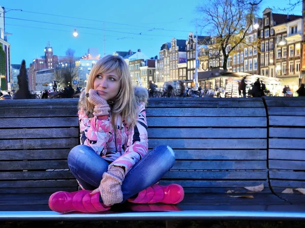Pembe ceket ve pembe çizme çevre canal Amsterdam mavi saat (akşam) bir bankta oturan üzgün Avrupa kız