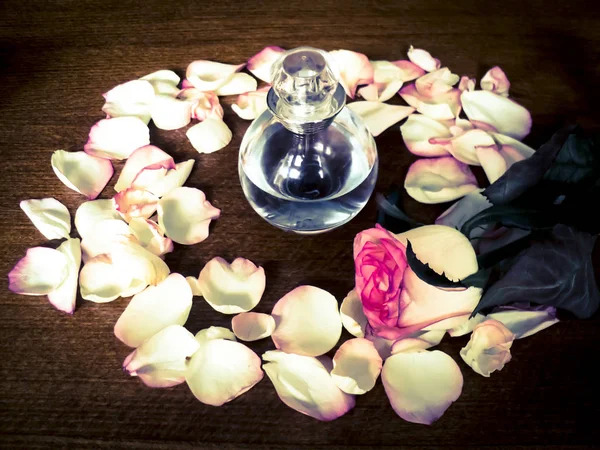 Flowers composition. One Glass perfume bottle in the center on the wood background, rose petals around. Rose flower lying down on the table — Stock Photo, Image