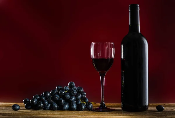 Botella de vino tinto, copas de vino y uvas sobre fondo rojo — Foto de Stock