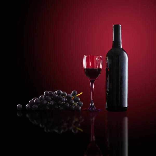 Botella de vino tinto, copas de vino y uvas sobre fondo rojo — Foto de Stock