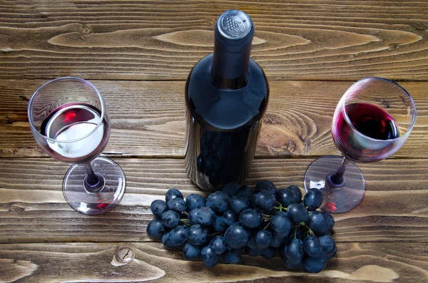 Botella de vino tinto, copas de vino y uvas sobre mesa de madera — Foto de Stock