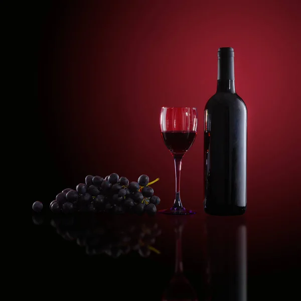 Botella de vino tinto, copas de vino y uvas sobre fondo rojo — Foto de Stock