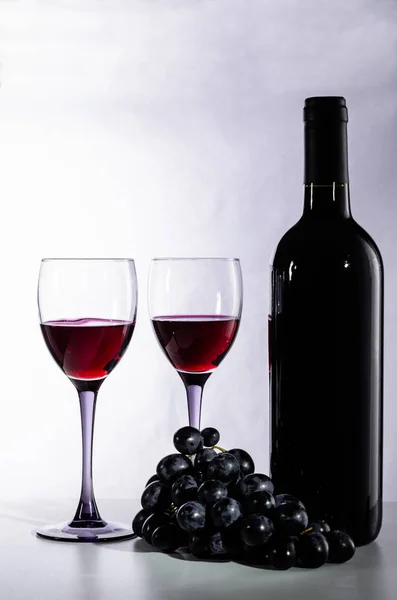 Botella de vino tinto, copas de vino y uvas sobre fondo lila — Foto de Stock