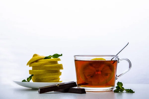Glass cup with tea, mint, chocolate and a cut lemon on a white background — Stock Photo, Image