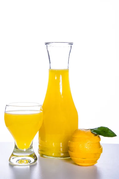 Decantador, vaso con zumo de naranja, naranja cortada sobre una mesa fresca y fondo blanco —  Fotos de Stock