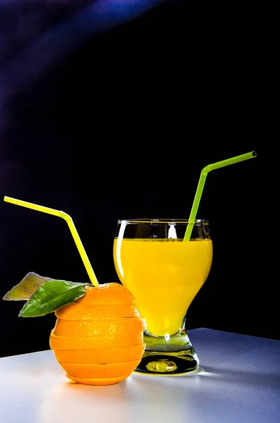 Glass with orange juice, a cut orange with a cocktail of straw on a black background — Stock Photo, Image