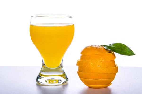 Vaso con zumo de naranja, una naranja cortada sobre una mesa fresca y un fondo blanco —  Fotos de Stock