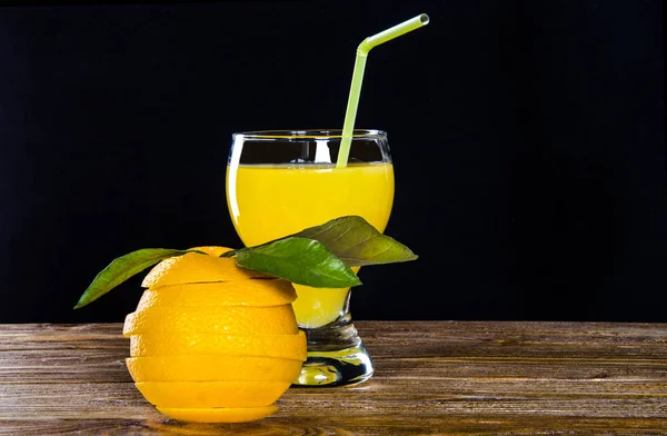 Vidro com suco de laranja, uma laranja cortada com um coquetel de palha em um fundo preto — Fotografia de Stock