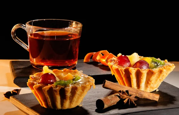 Taza de té con un pastel, canela y anís en bandeja y un fondo negro — Foto de Stock