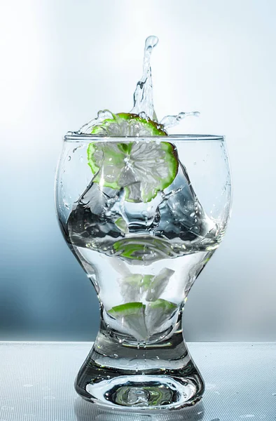 Bir kireç ve bej tonlarında bir şişe ile bir bardak suda sıçrama