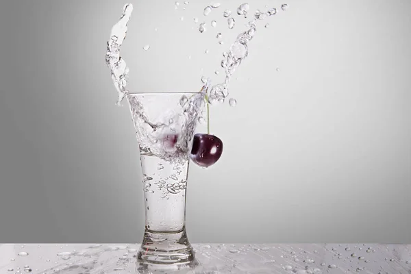 Gri bir arka plan üzerinde bir kiraz ile bir bardak suya bir sıçrama