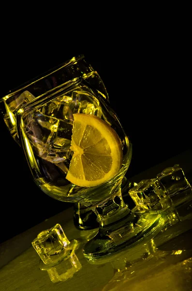 Дві склянки води, лимон і лід жовтого кольору на чорному тлі — стокове фото