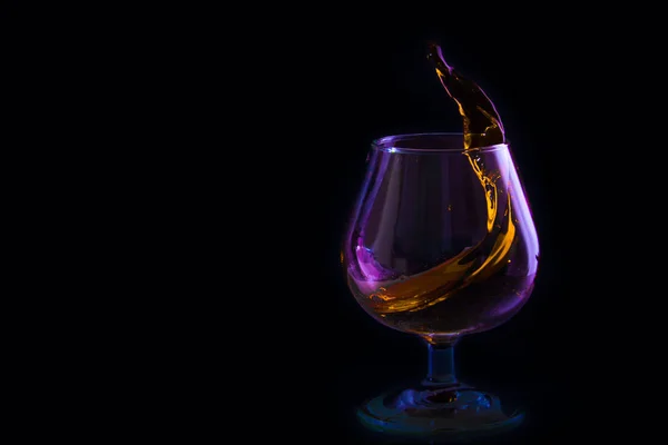 Salpicadura en una copa de brandy en la iluminación de color sobre un fondo negro — Foto de Stock